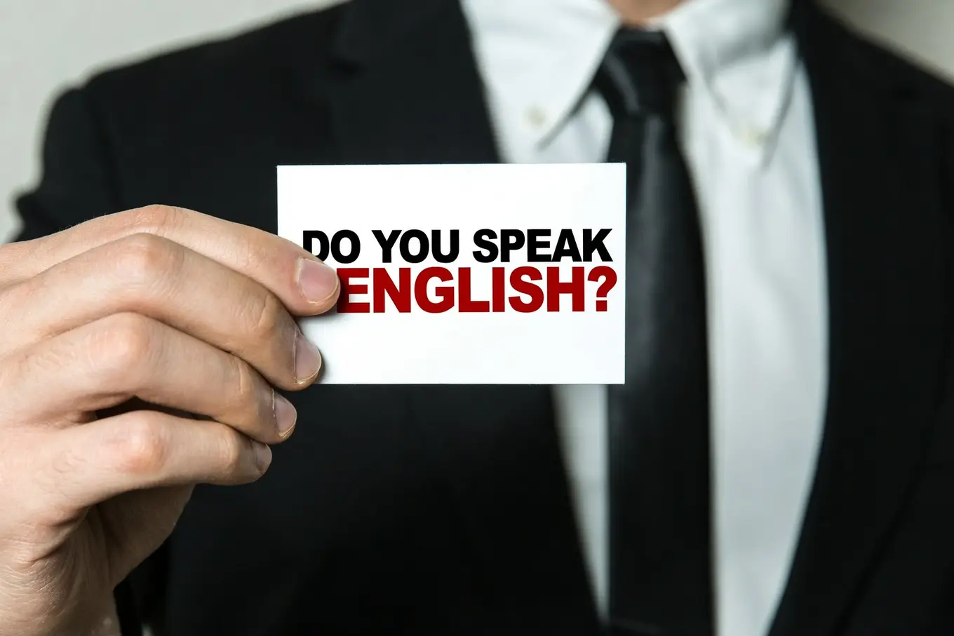 Mężczyzna w garniturze trzymający kartkę z napisem do you speak english?